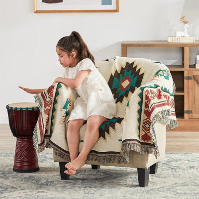 couverture de style sud-ouest dans les tons de blanc, bleu, brun et orange sur un fauteuil avec une jeune fille assise dessus.