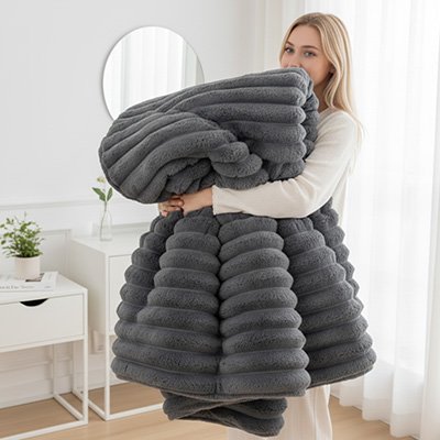 couverture grise dans les bras d'une femme qui sourit par la douceur et le confort du tissu